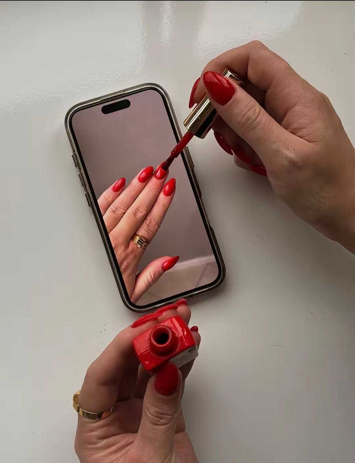 Red nail polish being applied, with a smartphone showing a matching manicure.