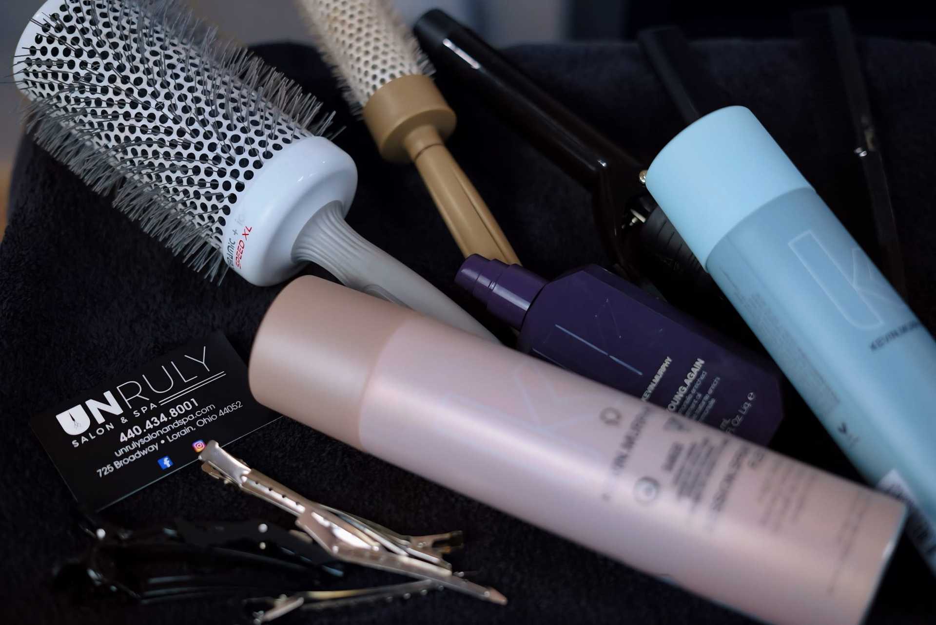 Salon hair styling tools and products, including brushes, clips, and sprays on a towel.
